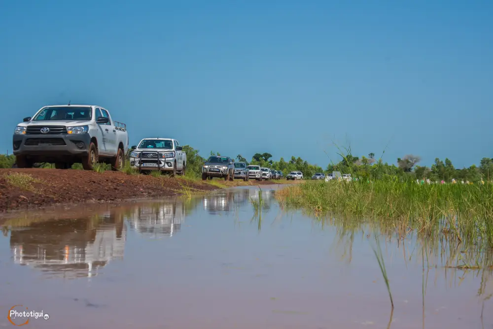 Convoy of white trucks on flooded dirt road during African Development Bank representatives' field visit